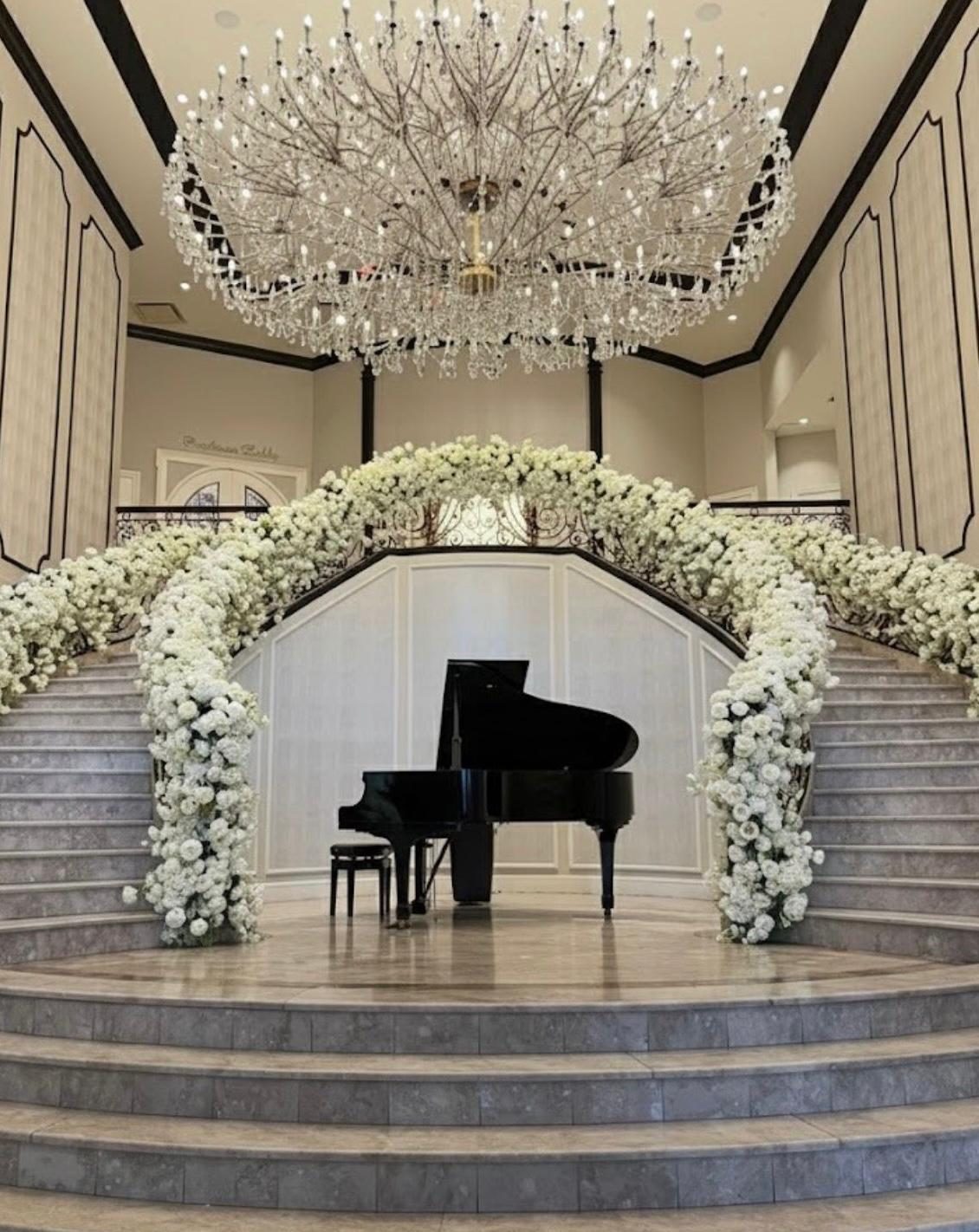 White floral staircase arch and chandelier over a grand piano in a Westchester wedding venue lobby