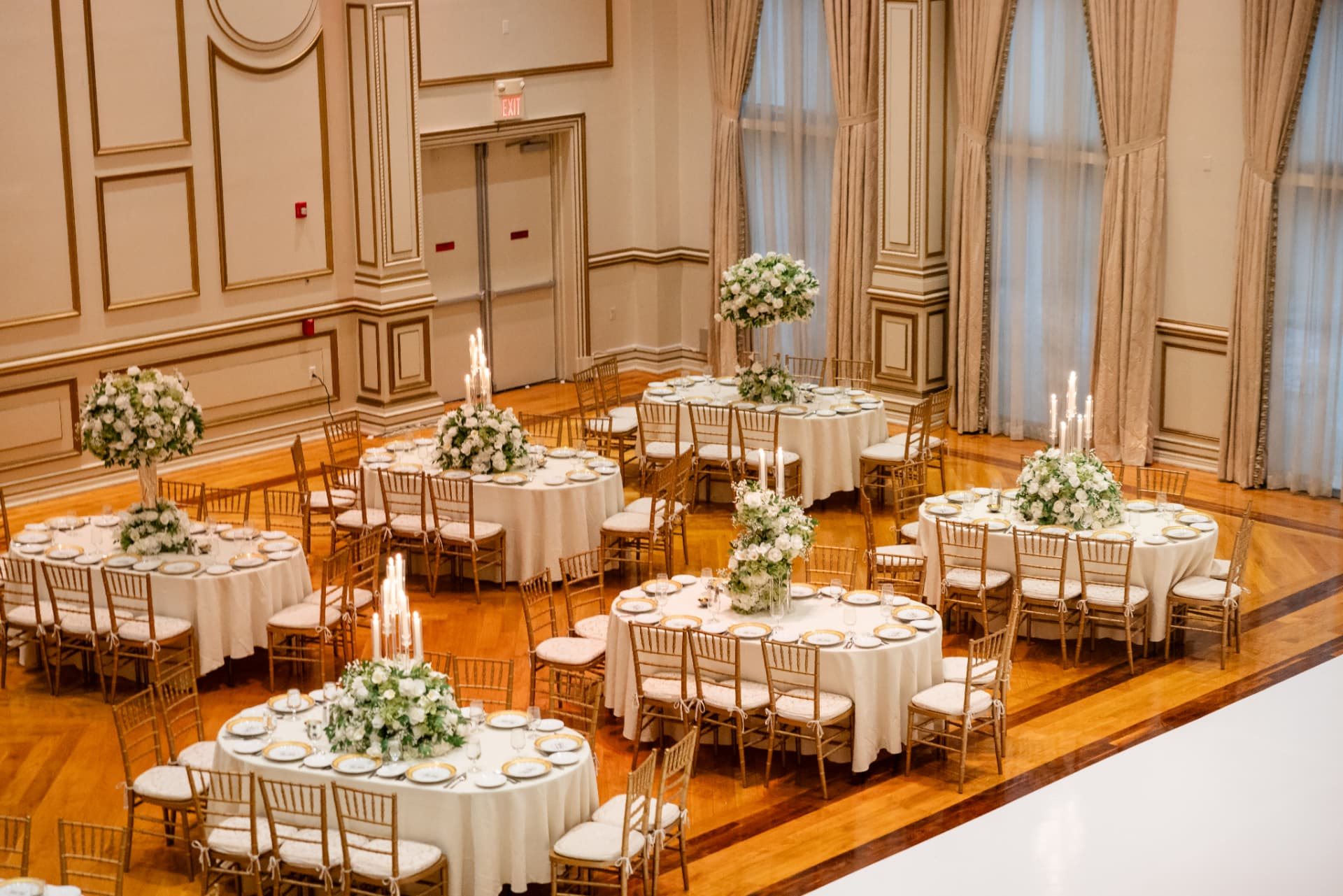 Paneled reception room seen from above, round tables with white and green centerpieces and gold chiavari chairs at The Tides Estate in North Haledon, New Jersey, designed by Let's Bloom Florist
